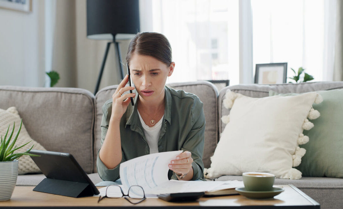 Mulher falando no telefone enquanto segura papéis, simbolizando ansiedade financeira.