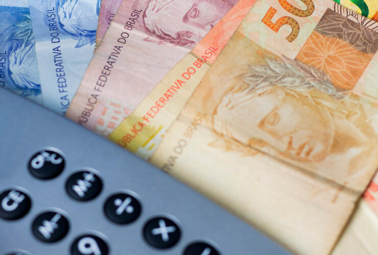 Notas de dinheiro ao lado de calculadora, representando o cálculo do décimo terceiro salário.