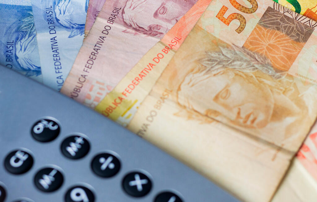 Notas de dinheiro ao lado de calculadora, representando o cálculo do décimo terceiro salário.