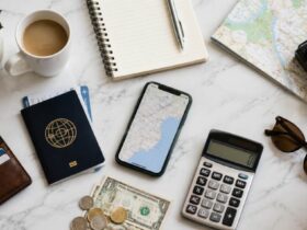 Como economizar em viagens? 3 Passaporte, moedas e notas de dinheiro, cadernos, mapas, canetas e calculadora, representando como economizar em viagens.