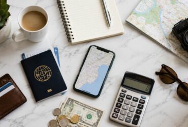 Passaporte, moedas e notas de dinheiro, cadernos, mapas, canetas e calculadora, representando como economizar em viagens.