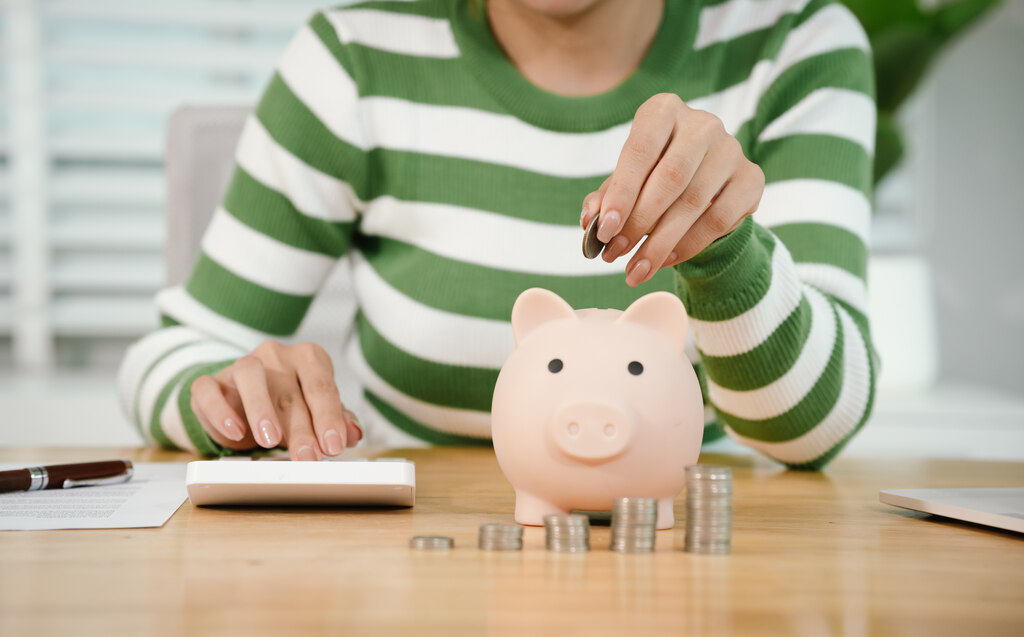 Pessoa calculando finanças pessoais e guardando dinheiro no cofrinho depois de entender como funciona aposentadoria privada na prática.