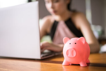 porquinho e pessoa ao fundo usando o notebook para pesquisar como juntar dinheiro ganhando pouco