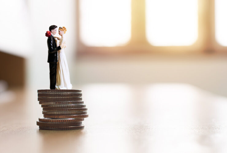 Casal de noivos em miniatura sobre uma pilha de moedas simbolizando planejamento financeiro e como juntar dinheiro para o casamento de forma estratégica.