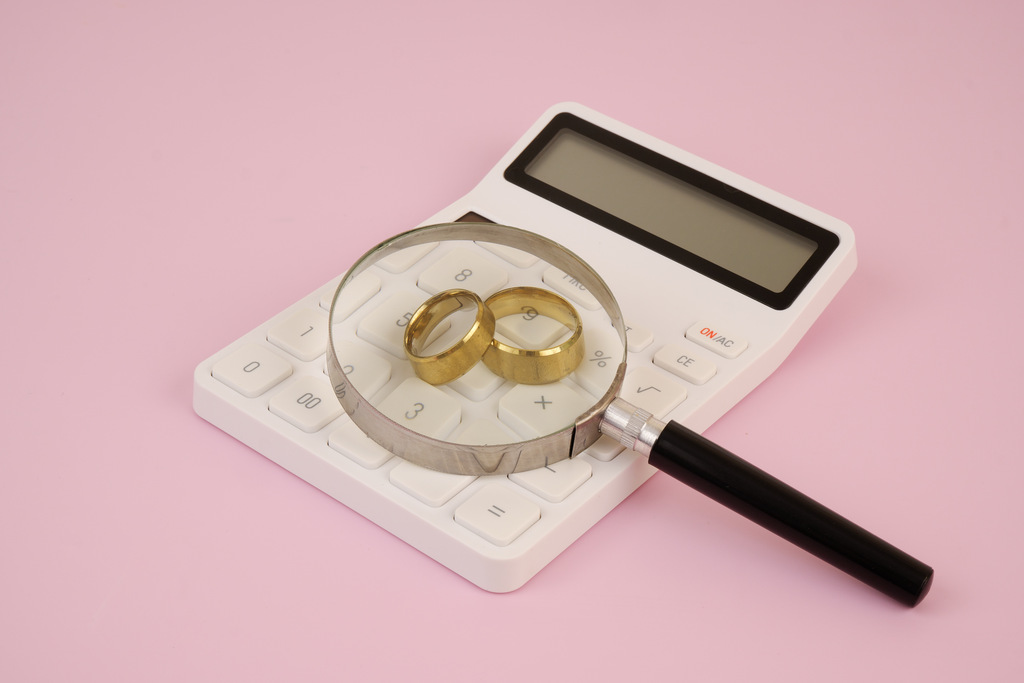Como juntar dinheiro para o casamento: guia completo para casar sem dívidas 2 Alianças de casamento sobre calculadora com lupa representando análise de custos e como juntar dinheiro para o casamento com controle financeiro detalhado.