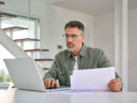 Homem analisando documentos e usando notebook, indicando a verificação de dívidas e como saber se meu nome está no Serasa.