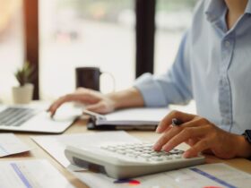 Pessoa usando calculadora e notebook ao mesmo tempo, organizando dados financeiros em uma mesa de trabalho, representando a rotina prática de controle de recebimento no dia a dia de pequenos negócios.