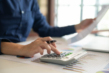 Pessoa usando calculadora e gráficos financeiros como ferramentas para controlar gastos.