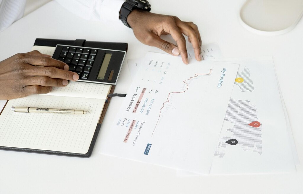 Pessoa analisando documentos financeiros em uma mesa com calculadora, gráfico de desempenho de portfólio e mapa com marcadores, representando o processo de avaliação de investimentos sustentáveis e tomada de decisões estratégicas.
