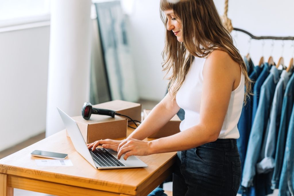 Limite de faturamento MEI: entenda o teto e evite surpresas 3 microempreendedora em sua loja de roupas, usando o computador para verificar o limite de faturamento MEI