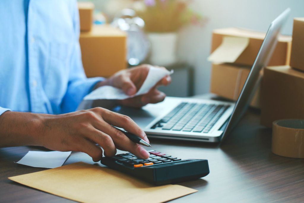 Limite de faturamento MEI: entenda o teto e evite surpresas 2 pessoa usando o notebook e calculadora para verificar o limite de faturamento MEI