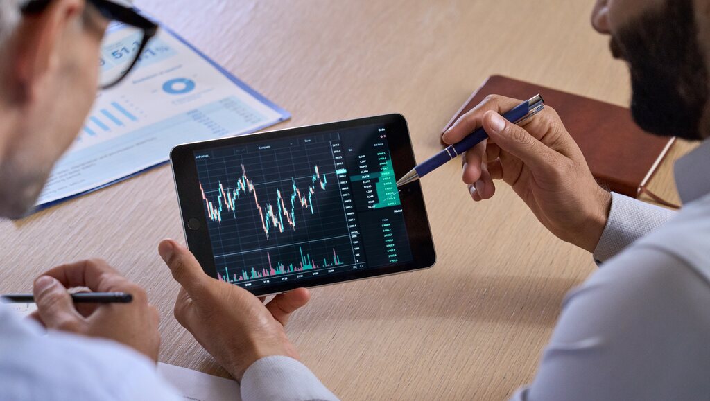 30 principais livros de investimentos para conhecer 2 pessoas visualizando gráfico em tablet, representando os livros de investimento