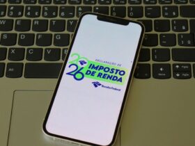 Malha fina do Imposto de Renda: erros mais comuns e como evitar 4 Um smartphone posicionado sobre o teclado de um laptop exibe em sua tela o logotipo oficial da Receita Federal para a declaração de IR 2026. A imagem ilustra a facilidade de acesso digital para acompanhar a situação da declaração e verificar se o contribuinte apresenta pendências que possam levá-lo para a malha fina do Imposto de Renda.