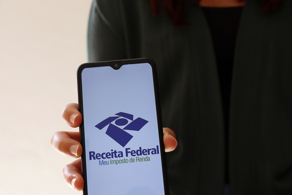 Pessoa segurando celular com aplicativo da Receita Federal aberto para envio da declaração de imposto de renda.