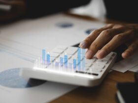Mão digitando em calculadora com gráficos flutuantes, representando análise de dados e planejamento tributário empresarial.