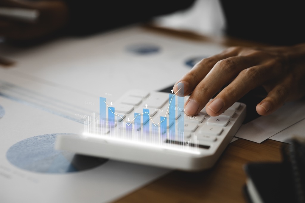 Mão digitando em calculadora com gráficos flutuantes, representando análise de dados e planejamento tributário empresarial.