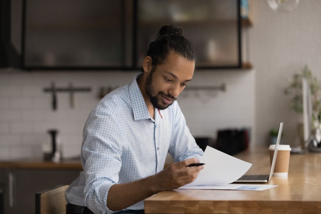 Profissional autônomo analisando documentos financeiros em casa, com expressão concentrada, enquanto realiza o controle de recebimento dos clientes de forma manual.