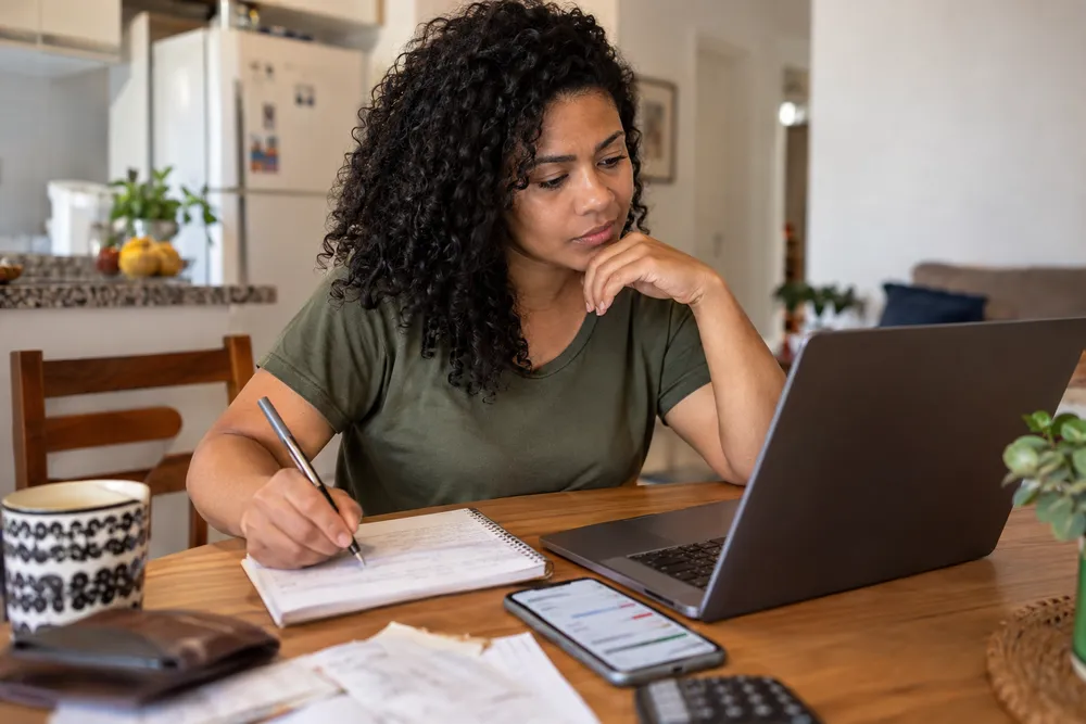 Mulher organizando contas no notebook para fazer uma projeção financeira do orçamento pessoal.