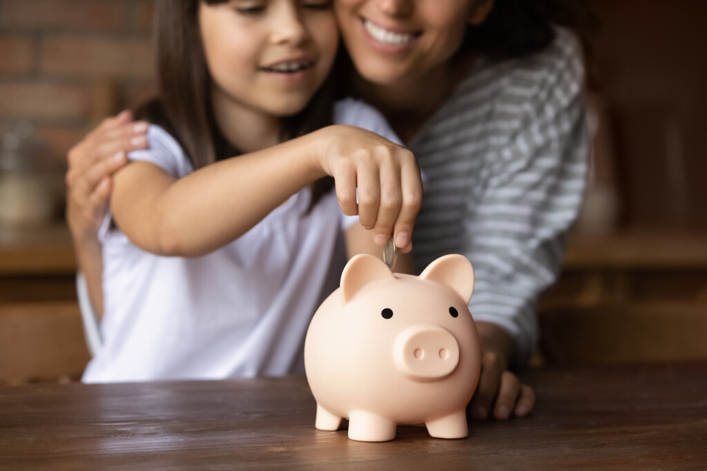 Como economizar dinheiro ganhando pouco? Veja 5 dicas estratégicas 3 mãe e filha adicionando moeda em porquinho representando como economizar dinheiro ganhando pouco