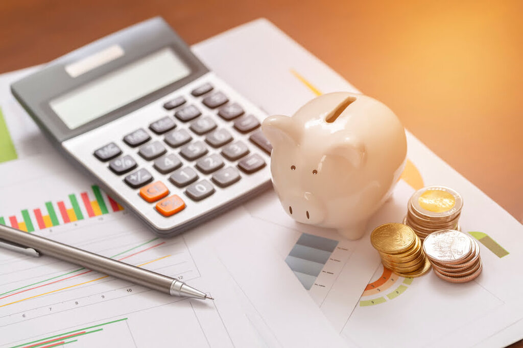 Entenda quanto rende a poupança e se vale a pena investir 3 porquinho ao lado de calculadora e moedas, representando quanto rende a poupança