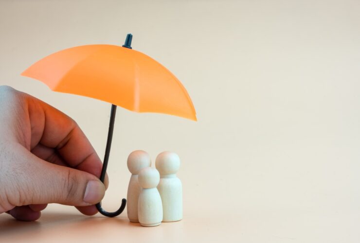 Mão segurando guarda-chuva laranja sobre figuras de família, simbolizando os tipos de seguros que oferecem proteção financeira e pessoal.