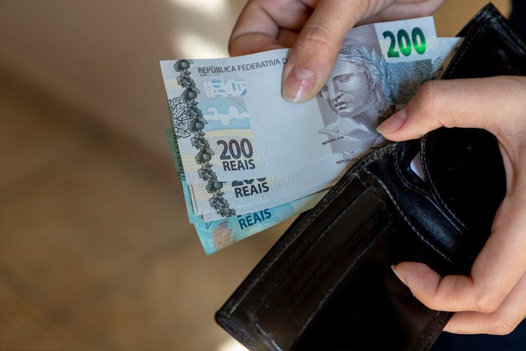 Tarifas bancárias: o que é, quais são e como minimizar os custos 2 Pessoa tirando dinheiro da carteira pensando nas tarifas bancárias
