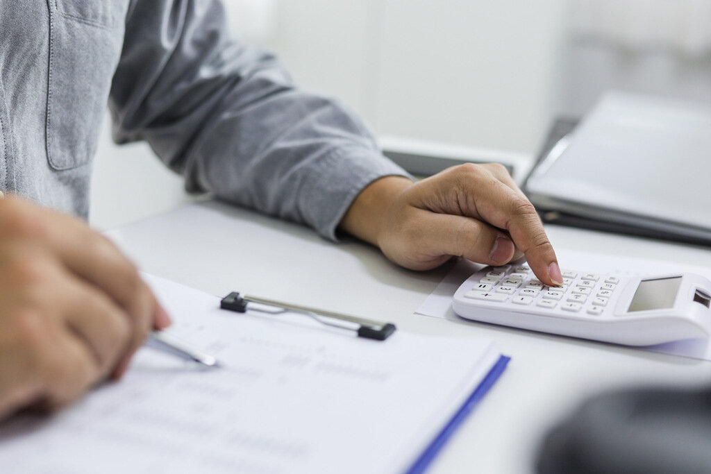 Empreendedor calculando tributos com papéis e calculadora na mesa, em processo de planejamento tributário. 
